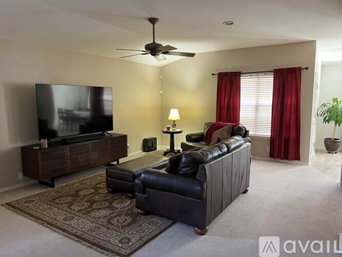 A living room with a black leather couch and a flat screen TV.
