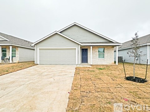 A house with a grey garage door and a small tree in front of it.