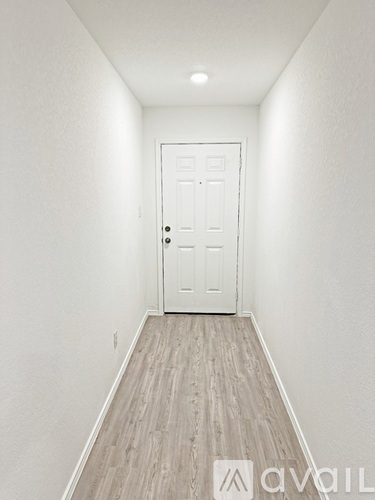 A white door is at the end of a hallway with wood flooring.