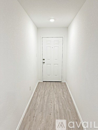 A white door is at the end of a hallway with wood flooring.