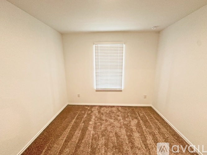 A room with a carpeted floor and a window with blinds.