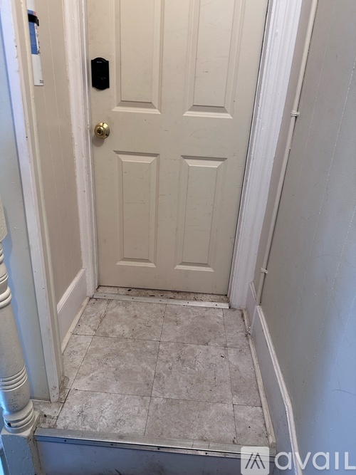 A white door with a black handle is in a white hallway.