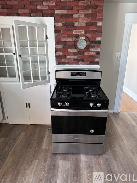 A stainless steel stove with a black top is in a kitchen with a brick wall and a white cabinet.
