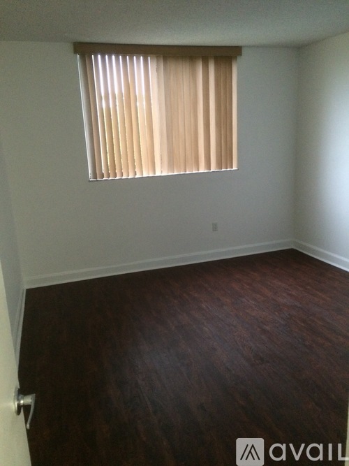 A room with a window covered by blinds and wooden flooring.