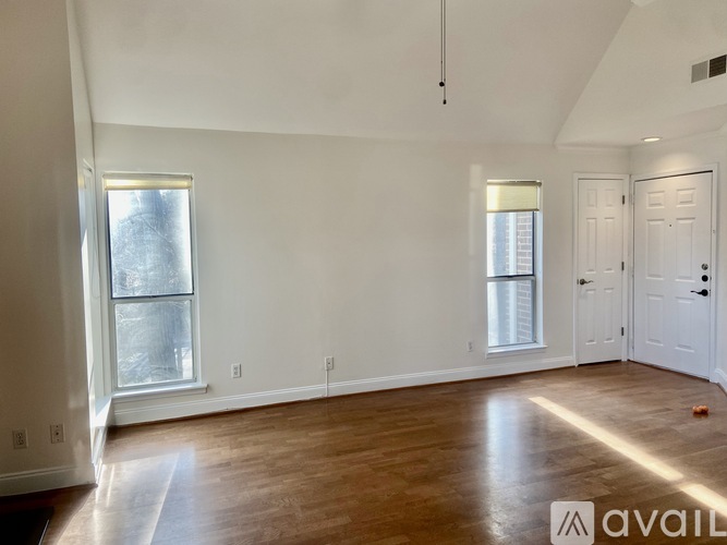 A spacious room with wooden floors and two windows.