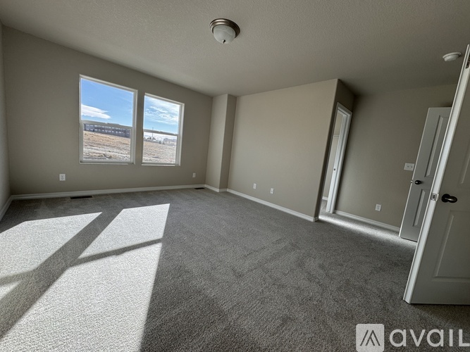 A spacious room with grey carpeting and a large window with a view of the outdoors.