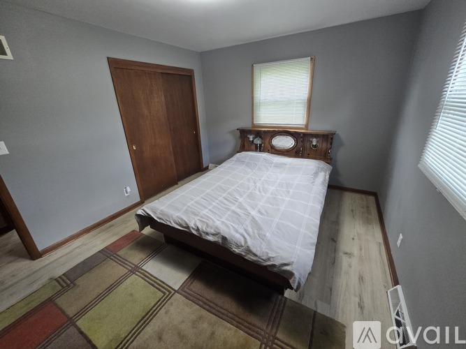 A bedroom with a bed, wooden door, and a window with blinds.