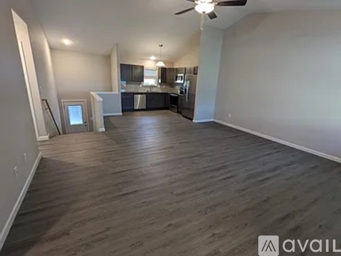A spacious living room with a kitchen in the background and hardwood floors.