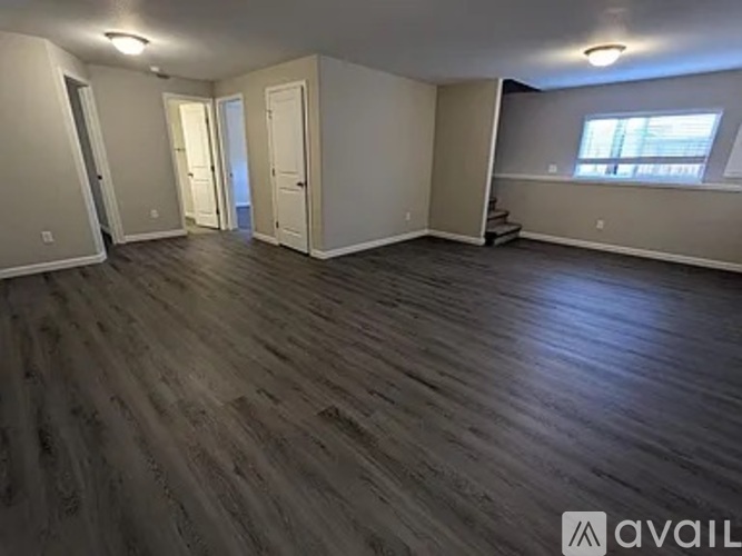 A spacious room with wooden flooring and white walls.