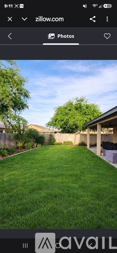 A grassy backyard with a house and trees in the background.