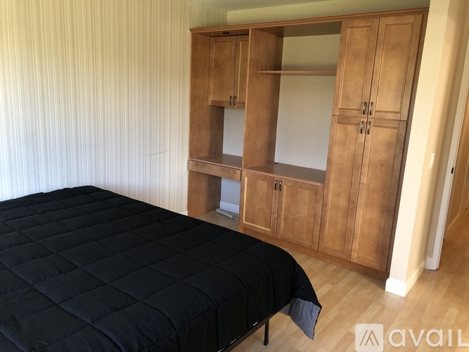 A bed with a black cover sits in a room with wooden cabinets.