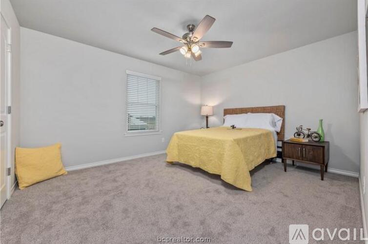 A bedroom with a bed, a ceiling fan, and a nightstand with a bicycle on it.