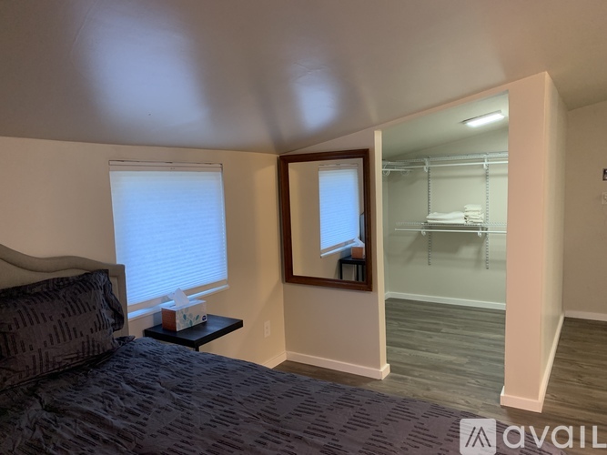A bedroom with a bed, a window with blinds, a nightstand with a lamp, and a closet with a mirror.