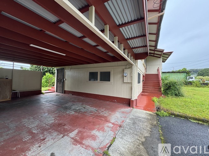 A covered parking area with a red floor and a white building.