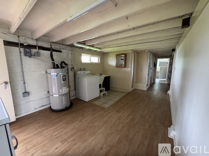 A spacious room with wooden flooring and white walls, containing a water heater and a fridge.