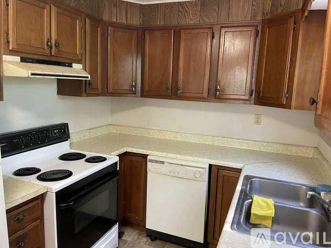 A kitchen with a white stove top oven, a white dishwasher, and wooden cabinets.
