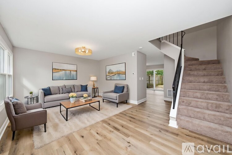 A living room with a brown sofa, a grey armchair, a coffee table, and a staircase.