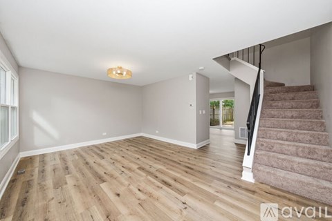 A spacious room with wooden flooring and a staircase leading to another room.