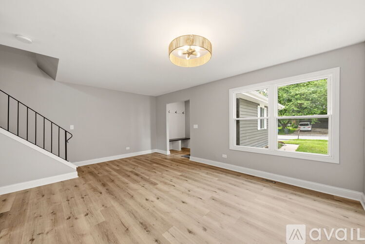 A room with wooden flooring and a large window showing a view of a house and trees.