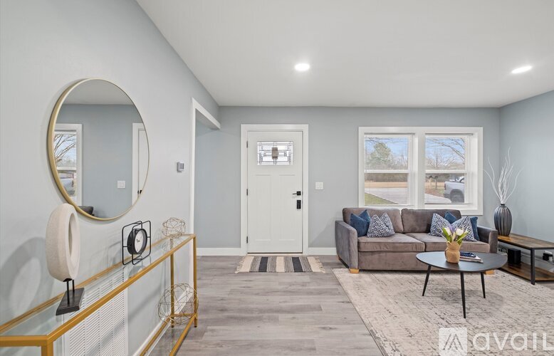 A living room with a grey couch, a round mirror, a coffee table, and a glass table with a vase on it.