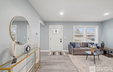 A living room with a grey couch, a round mirror, a coffee table, and a glass table with a vase on it.