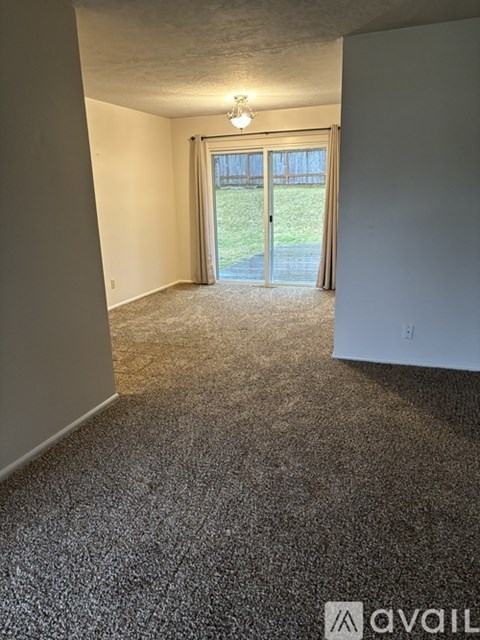 A room with a carpeted floor and a sliding glass door leading to a grassy area.