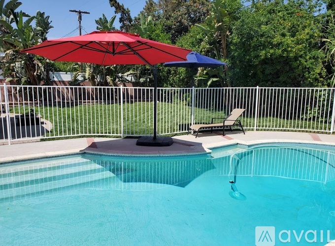 A red umbrella is above a pool with a white fence around it.