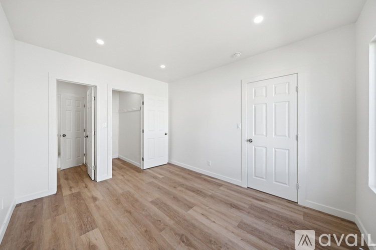 A room with white walls and wooden flooring, with a door on the right and two open doors on the left.