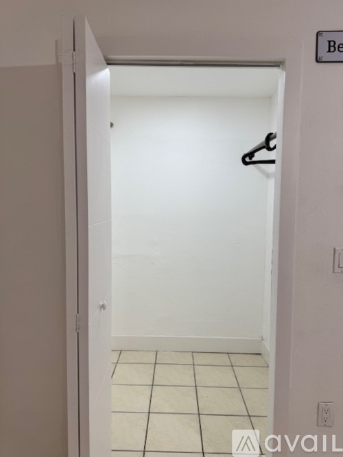 A white door is open to a room with a black coat hanger.