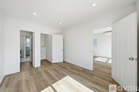 A spacious room with white walls and wooden flooring, featuring a white door and a white cabinet with a mirror.