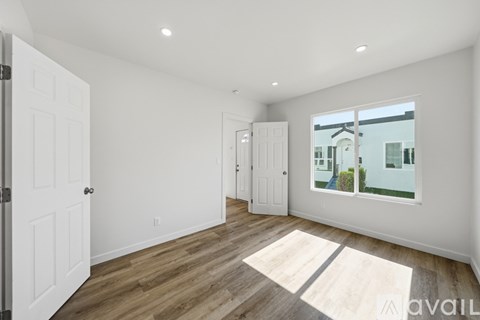 A room with white walls and wooden flooring, with a large window showing a view of a building outside.