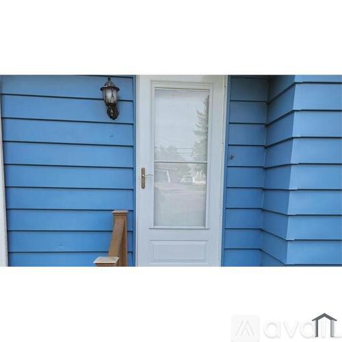 A white door with a glass window is on a blue house.