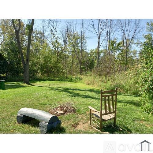 A wooden chair sits on a grassy area next to a log and a tree.