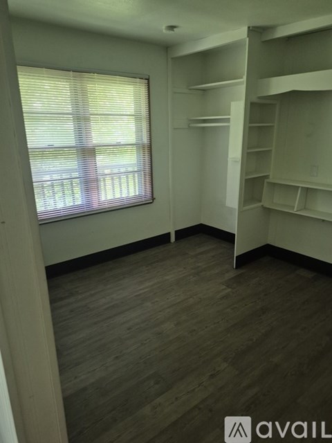 A room with wooden floors and white walls, featuring a window with blinds and a bunk bed.