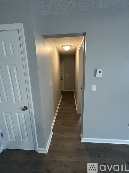 A hallway with a white door on the left and a light switch on the wall on the right.