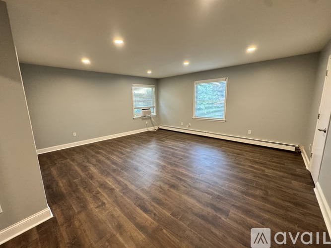 A room with wooden flooring and two windows.