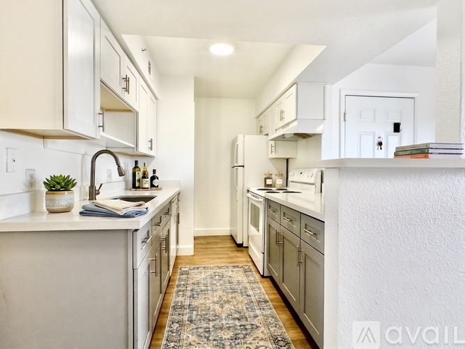 A kitchen with white cabinets and appliances, a rug on the floor, and a doorway leading to another room.