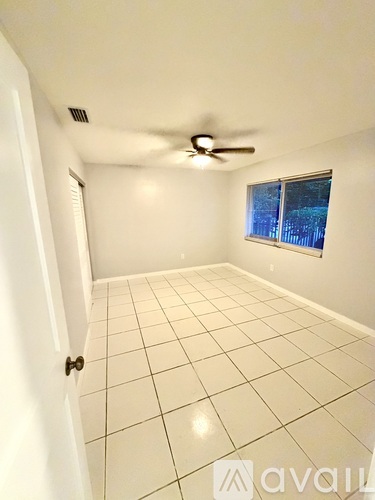 A room with a ceiling fan and a window showing a view of trees outside.