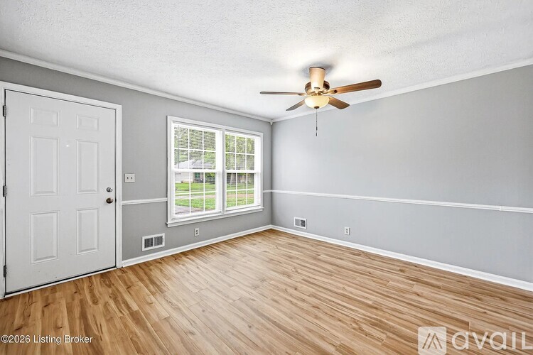 A room with a ceiling fan and a window overlooking a lawn.