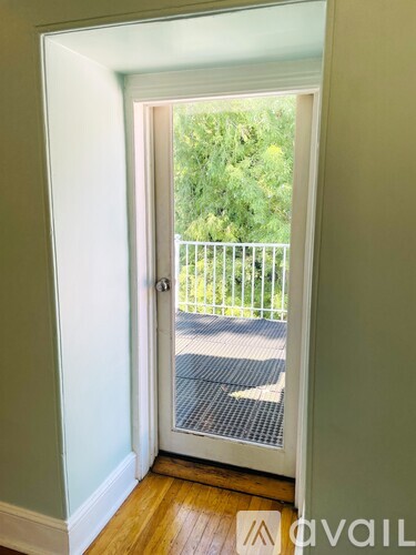 A doorway leading to a balcony with a view of a street and trees.