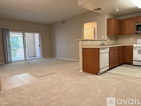 A kitchen with wooden cabinets and appliances in a room with carpeted flooring and a sliding glass door.