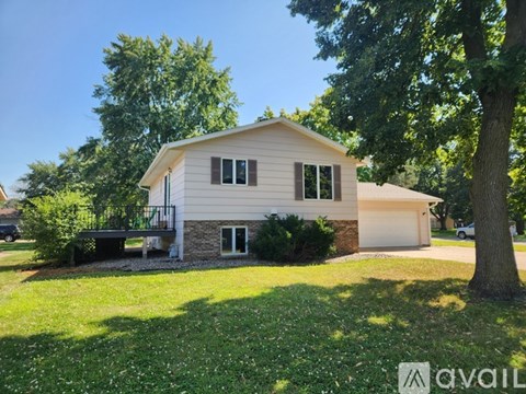 A house with a white siding and a brown roof is surrounded by greenery.