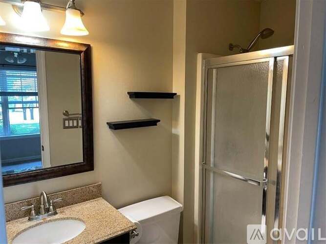 A bathroom with a toilet, sink, mirror, and a shower door.