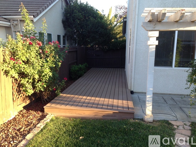 A backyard with a wooden deck and a white house.