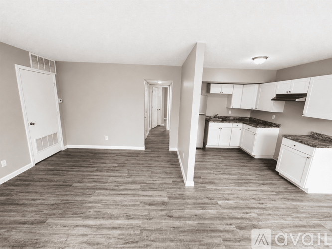 A spacious kitchen and living room with white appliances and wood flooring.