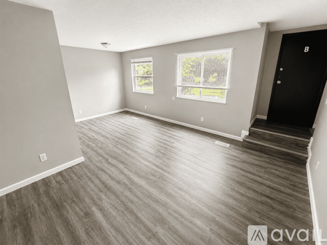 A spacious room with wooden flooring and two windows.
