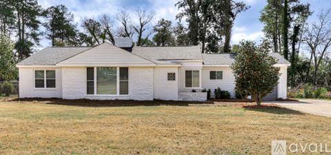 A white house with a grey roof and a tree in front of it.