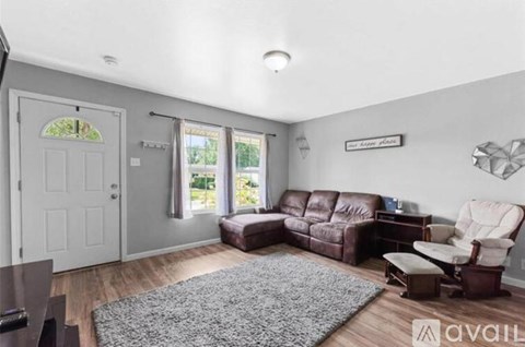 A living room with a brown leather couch and a grey rug.