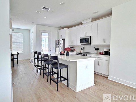 A kitchen with white cabinets and a white island with black chairs.