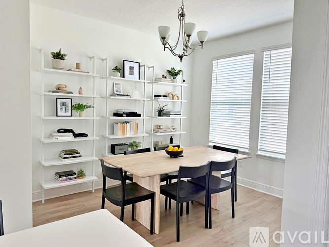 A dining room with a wooden table and chairs, a chandelier, and a bookshelf with various items.